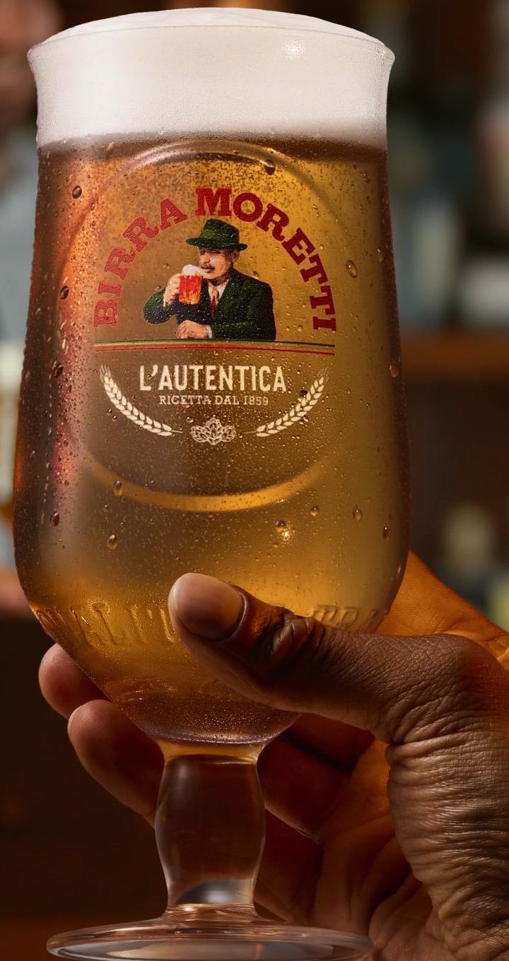A glass of Birra Moretti held up at the bar